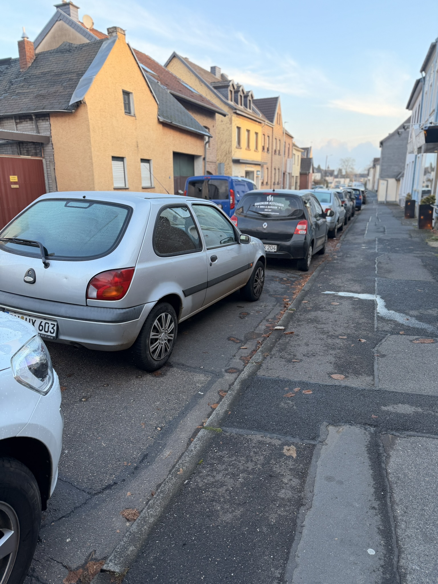 Straßenansicht mit einem beschrifteten Smoker-Kitchen-Lieferfahrzeug und weiteren parkenden Autos